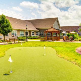 A scenic view of a putting green in front of a residential building, surrounded by well-maintained gardens and outdoor seating areas.