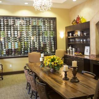 A stylish dining room featuring a large wine display, elegant chandelier, and a wooden table adorned with decorative candles and flowers.