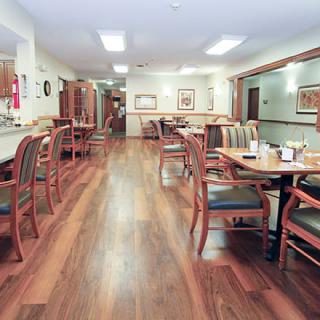 A spacious dining area with wooden tables and chairs, featuring a polished hardwood floor.