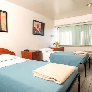 A simple hotel room with two single beds, decorated with light blue bedspreads and minimal artwork on the walls.