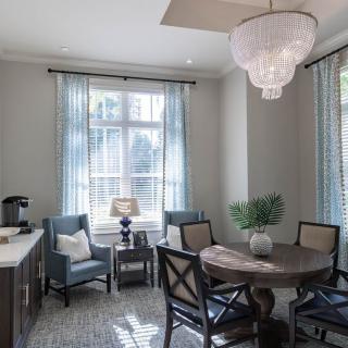 A modern dining room with ample natural light, featuring a round table, elegant chandelier, and comfortable seating.