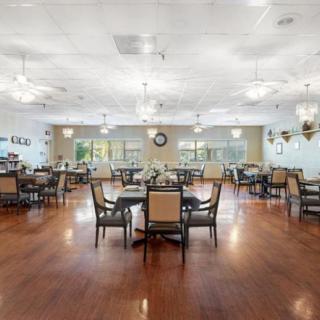 A spacious dining room with neatly arranged tables and chairs on a wooden floor, illuminated by ceiling lights.