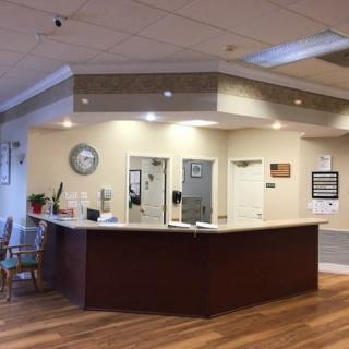 A spacious reception area with a central desk and waiting chairs, featuring a clock and well-lit ceiling.