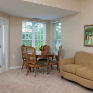 A cozy living room with a dining area featuring a round table and chairs, a beige couch, and large windows bringing in natural light.