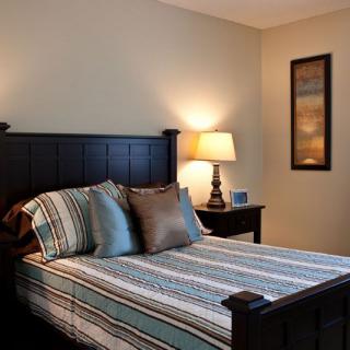 A cozy bedroom with a neatly made bed, a bedside table with a lamp, and warm lighting.