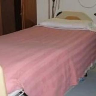 A hospital bed with a pink blanket in a medical room.