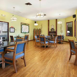 A well-lit dining room with wooden flooring, featuring tables and chairs arranged neatly.