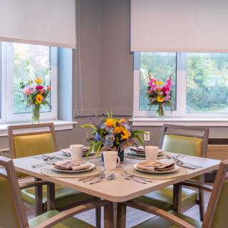 A beautifully set dining table with vibrant floral arrangements near large windows.