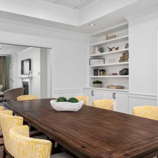 A modern dining room with a long wooden table and yellow chairs, featuring built-in shelves with decorative items.