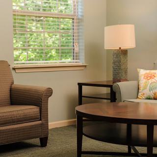 A cozy living room setting with a chair, sofa, and lamp near a window.