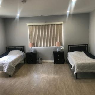 A minimalist bedroom with two twin beds, each accompanied by a nightstand and lamp, under window blinds.