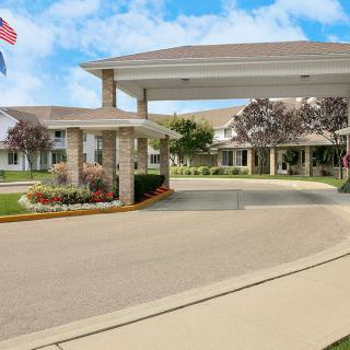 A welcoming entrance with a driveway and landscaped gardens under a sunny sky.