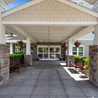 Covered entrance of a building with benches and plants.