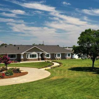 A beautiful house with a large green lawn and a winding driveway under a clear blue sky.