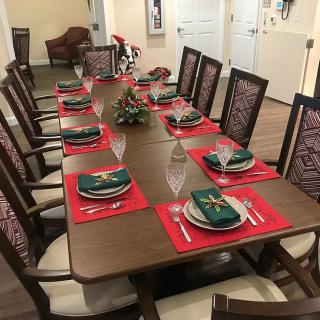A neatly set dining table with red placemats and green napkins, surrounded by chairs.