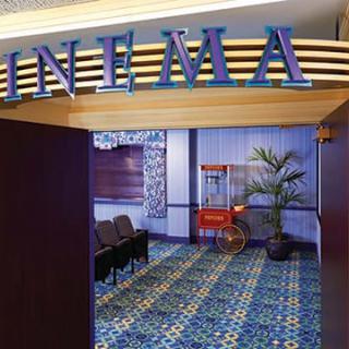 Entrance to a cinema with seating and a popcorn machine along the carpeted hallway.