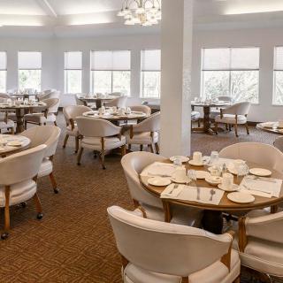 A spacious, elegantly designed dining room with neatly arranged tables and chairs, featuring large windows that allow natural light to brighten the space.