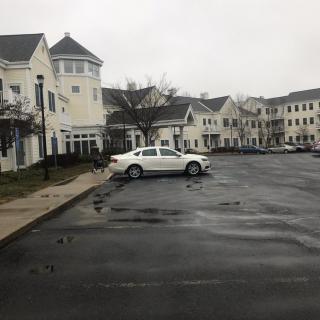 A parking lot with wet pavement in front of apartment buildings on a cloudy day.