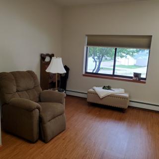 A minimalist living room with an armchair, ottoman, and a large window letting in natural light.