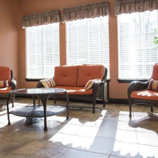 A bright living room with orange cushioned furniture and large windows letting in natural light.
