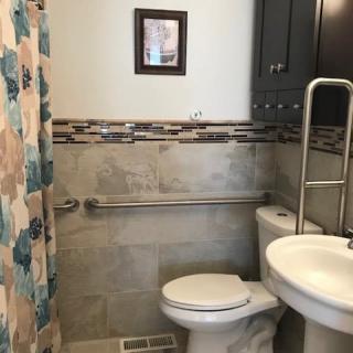 A small bathroom with a toilet, sink, and shower curtain. The walls are tiled and there is a grab bar next to the toilet.