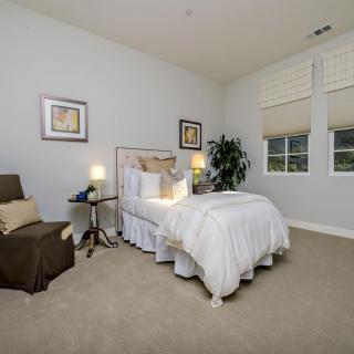 A cozy bedroom with a neatly made bed, comfortable chair, and warm lighting.