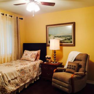 A cozy bedroom with a single bed, recliner chair, and soft lighting.