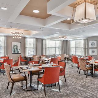A modern restaurant dining area with neatly arranged tables and red chairs under stylish ceiling lights.