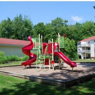 A sunny playground featuring red slides surrounded by green grass and trees.