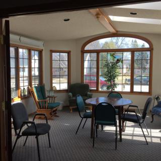 A cozy sunlit sitting area with multiple chairs and a round table, surrounded by large windows.