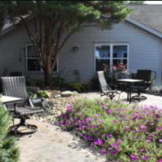 A peaceful garden patio with chairs and a table surrounded by flowers.