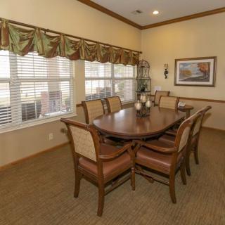 A traditional dining room setting with a wooden table, surrounded by chairs, and features large windows with decorative curtains.