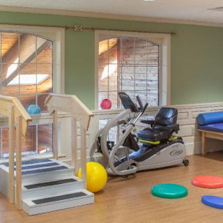 A rehabilitation room equipped with exercise tools including a stationary bike, stairs, therapy balls, and balance pads.