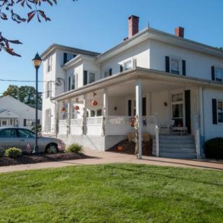 A large white residential house with a porch and a well-manicured lawn on a sunny day.