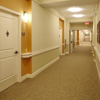 A long hallway in a building with multiple doors and carpeted flooring.