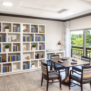 A cozy reading area with a bookshelf, table, and chairs next to a window.
