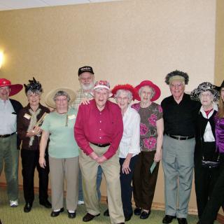 A group of seniors wearing various hats poses together indoors.