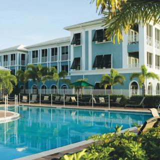 A tropical resort featuring a large swimming pool surrounded by palm trees and a multi-story building.