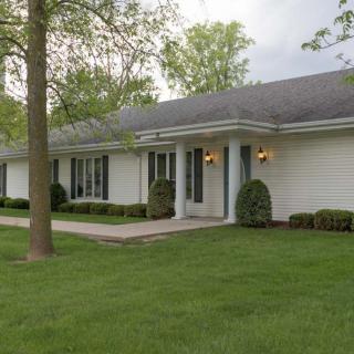 A single-story residential house with a well-maintained lawn and surrounding trees.