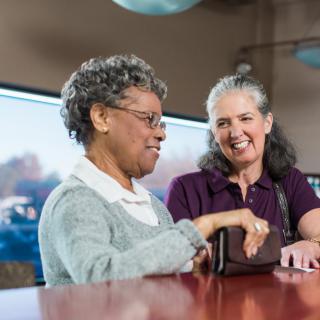 Two senior women smiling and enjoying a conversation indoors.