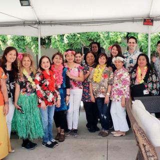 A group of people posing together at an outdoor event with a Hawaiian theme, wearing colorful leis and floral prints.