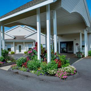 A well-maintained building entrance with a landscaped garden and covered driveway.