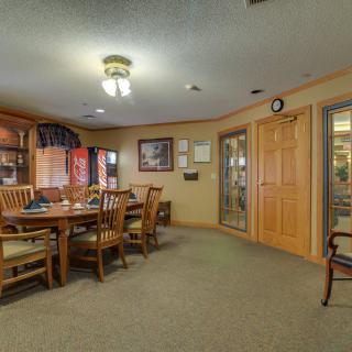 A cozy dining room with wooden furniture and bookshelves, illuminated by ceiling lights.