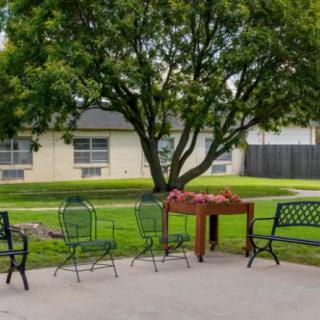 A peaceful backyard patio with chairs and a table under a lush tree.