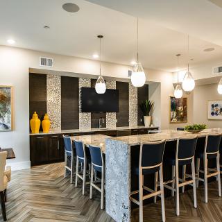 A modern kitchen with a large island, surrounded by bar stools and illuminated by pendant lights.