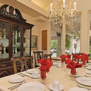 An elegantly set dining table with red napkins and a chandelier overhead.