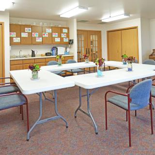 A brightly lit community center meeting room with arranged tables and chairs.