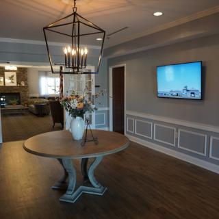 A stylish living room interior featuring a round table with a vase of flowers, a modern chandelier, and a wall-mounted television.
