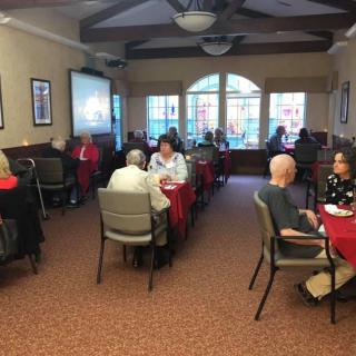 A group of people are seated around tables in a dining room, participating in a social gathering.