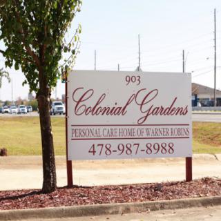 A sign for Colonial Gardens, displaying contact details and location.